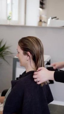 Saçını kuaförde yaptıran genç bir kadın. Güzel bir kadının koyu sarı saçlarını tarayan kuaför. Müşteri sandalyede oturup aynaya bakıyor. Kuaför, iş konsepti görüntüleri