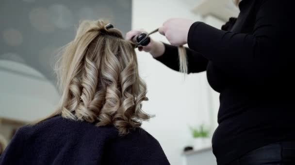 罕见的美发师使用专业的设备 卷曲的铁 为固定的客户做发型 美容院里年轻的黑发女子卷曲的头发 — 图库视频影像
