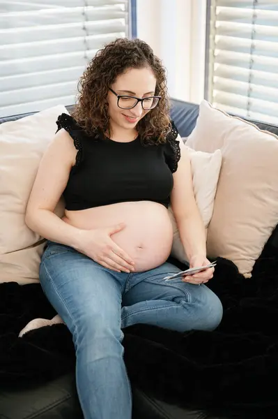 一个快乐的孕妇摸着肚子 看着坐在沙发上的超声波的垂直照片 怀孕的概念 — 图库照片