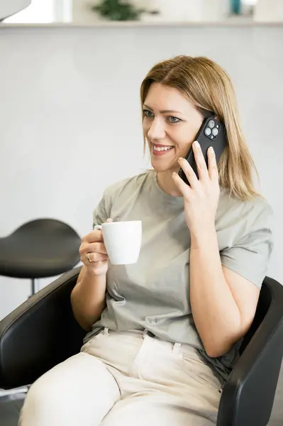 Genç Mutlu Bir Kadın Kuaförde Oturuyor Saçını Yaptırıyor Cep Telefonuyla — Stok fotoğraf