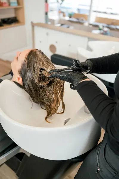 side front view of hairdresser giving a head massage to a caucasian woman client with her eyes closed while washing her hair soaping in the sink. beauty and haircare concept