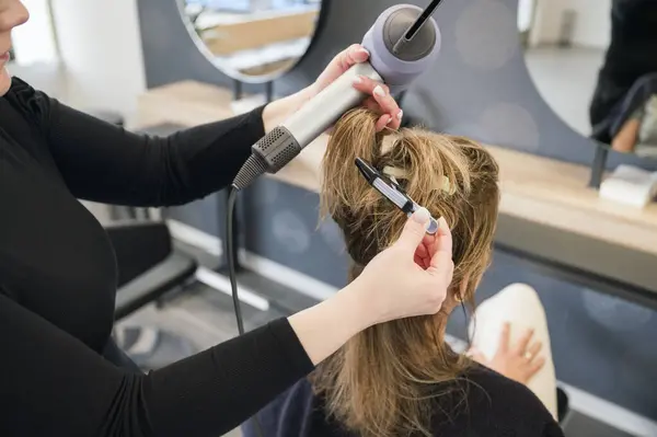 unrecognizable stylist is drying a womans hair with a blow dryer, woman sitting in chair, looking in mirror. unrecognizable hairdresser working in beauty salon.