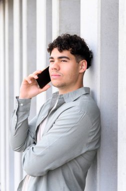 Ciddi yakışıklı genç işadamı cep telefonunu açık havada kullanıyor ve güneşli bir günde mesafeye bakıyor. Adam şehir caddesinde telefon görüşmesi yapıyor. iş kavramı