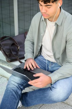 Genç erkek öğrencilerin günlük kıyafetlerini giyip dışarıda dizüstü bilgisayarla oturup online açık hava adamı eğitimi alırken sokak e-öğreniminde uzaktan çalışmayı öğrenmeleri. Kentsel yaşam tarzı kavramı