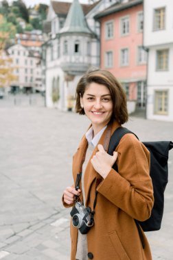 Kameraya gülümseyen genç bir bayan turistin dikey portresi boynundan ve kışlık kıyafetlerinden sarkan bir kamerayla.