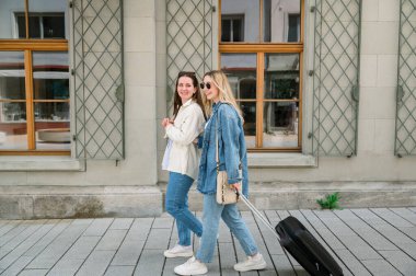 Avrupa 'da tatil boyunca valiz taşıyan beyaz tenli iki kadın turist..