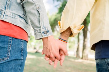 Tanınmayan eşcinsel çift, gurur bileziği takıyor, el ele tutuşuyor, LGBT gökkuşağı bileziği, çeşitlilik ve LGBTQ kavramına sahip tanınmayan homoseksüel erkek çiftin elleri.