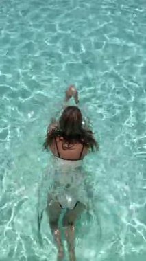 Yukarıdan yüzme havuzunda uzun saçlı, tanınmayan aktif bir kızın hava aracı görüntüsü, mavi suda yüzen genç bir kadın, tropikal tatil, tatil konsepti.