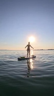 Mayo giyen genç bir kadın gün batımında Almanya 'da Bodensee' de bir kürek tahtasından atlıyor.
