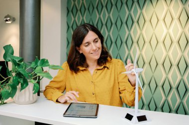 35-39 yıllık iş kadını, yel değirmeni, rüzgar türbini modeli ile birlikte dijital tablet kullanıyor, belgeleri analiz ediyor, yeniden kullanılabilir enerji projesi üzerinde çalışıyor. iş kavramı
