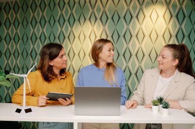 Gündelik kıyafet giyen, modern ofis çalışma alanında birlikte çalışan ve yenilenebilir enerji projesini tartışan bir grup kadın iş adamı. iş kavramı