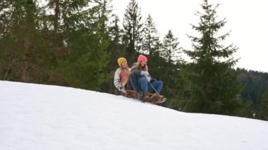 Genç, neşeli bayan arkadaşlar kışlık kıyafetler giyip kışın karlı bir tepeden kayarak kayarak dağlarda gülüyorlar. kış konsepti