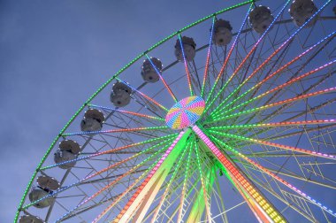 Parlak bir dönme dolap. Gece renkli LED ışıkları var. Canlı bir panayırda gökyüzüne doğru yükselerek canlı ve neşeli bir atmosfer yaratıyor.