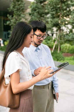 İyi giyimli, omuz çantalı Asyalı genç bir kadın ve ofis binasının önünde duran erkek meslektaşları, elinde tablet, grafikleri gösteriyor, Bangkok 'taki yeni projelerden bahsediyorlar. Yüksek kalite fotoğraf