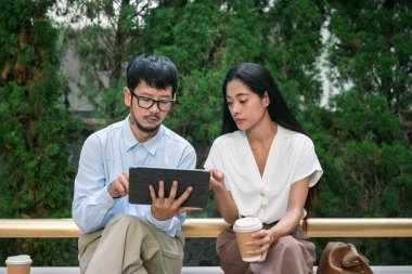 Asyalı iş adamları, dışarıda bir bankta oturan meslektaşlar, yeni iş projeleri hakkında konuşmalar, beyin fırtınaları. İş adamı Bangkok Tayland 'da dizüstü bilgisayarda yeni projeyi açıklıyor. iş kavramı