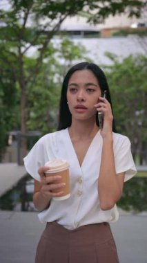 Ciddi Asyalı kadın profesyoneller, iş kıyafetleri içinde, şehir ortamında yönetici, kahve içiyor, Bangkok Tayland 'da binanın dışında akıllı telefondan konuşuyor. iş kavramı