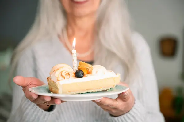 Gülümseyen ve elinde bir dilim limonlu pasta tutan, 60. yaş gününü mum ışığında kutlayan, kilometre taşı, sevinç ve uzun yaşamı sembolize eden son sınıf öğrencisi kadın. yaşam tarzı konsepti