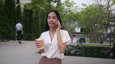 Neşeli Asyalı kadın profesyoneller, iş kıyafetleri içinde, şehir ortamında yönetici, kahve içiyor, Bangkok Tayland 'da binanın dışında akıllı telefondan konuşuyor. iş kavramı