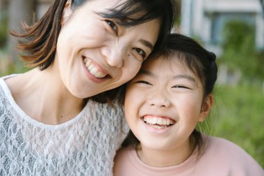 Gülümseyen Asyalı, Japon, Koreli, anne ve kızının portresi. Birlikte hassas bir anın tadını çıkarıyorlar, gülümsüyorlar, mutluluk saçıyorlar ve aile sevgisini açık hava sahnesinde paylaşıyorlar. Ebeveynlik kavramı