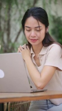 Bangkok Kafe 'sinde çalışan kadın profesyonel, dijital iş akışı sırasında ergonomik rahatsızlığı ve nazik kendine masajı ele alıyor.