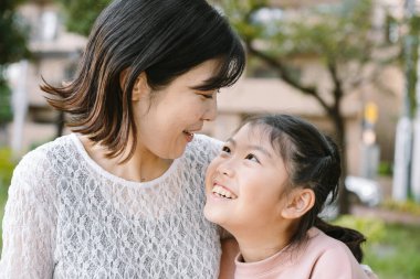 Günlük kıyafetlerle gülümseyen anne ve kız, birbirlerine bakıyorlar, birlikte özel bir anın tadını çıkarıyorlar, aile bağlarının iç açıcı bir sahnesi yaratıyorlar, açık havada aşk yaşıyorlar. aile kavramı
