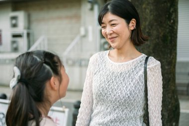 Japon anne, Japonya 'nın büyüleyici bir caddesinde kızıyla konuşurken içten bir gülümseme sergiliyor. Gerçek bağlarını ve mutlu aile hayatlarını sergiliyor.