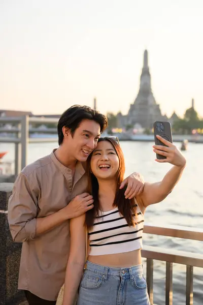 Genç Asyalı turistler Bangkok 'ta tatillerinin tadını çıkarıyorlar. Arka planda ünlü Wat Arun tapınağıyla selfie çekiyorlar. Gün batımında unutulmaz bir anı yakalıyorlar.
