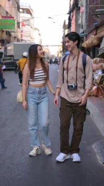 Genç Asyalı çift, el ele tutuşuyor, Bangkok 'un hareketli sokaklarında geziniyor, seyahat maceraları sırasında hareketli atmosferin ve yerel dükkanların tadını çıkarıyorlar. yaşam tarzı konsepti