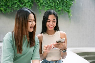 İki neşeli genç bayan arkadaş, Bangkok, Tayland 'ın canlı atmosferiyle çevrili akıllı bir telefonla sosyal medyada gezinirken gülüp eğleniyorlar. yaşam tarzı konsepti