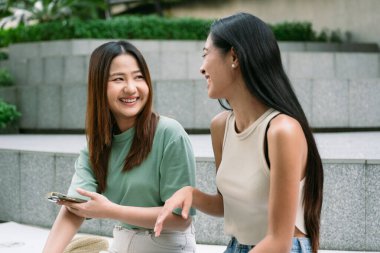 İki genç bayan arkadaş Bangkok 'ta merdivenlerde oturuyor, birlikte gülüyor ve gülüyorlar, biri akıllı telefon tutuyor, bir anlık bağlantının ve arkadaşlığın tadını çıkarıyorlar. yaşam tarzı konsepti