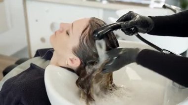 Kuaförün, saçlarını lavaboda yıkarken gözleri kapalı, beyaz bir kadın müşteriye kafa masajı yaparken yan görüntüsü. güzellik ve saç bakım konsepti