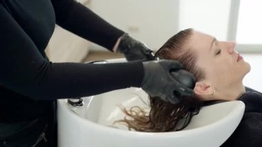 Saç stilistinin onları yıkadıktan sonra rahatlamış kadın saçlarını taramasının yan görüntüsü. Kuaförün yanındaki sandalyede oturan kadın. güzellik ve saç bakım konsepti