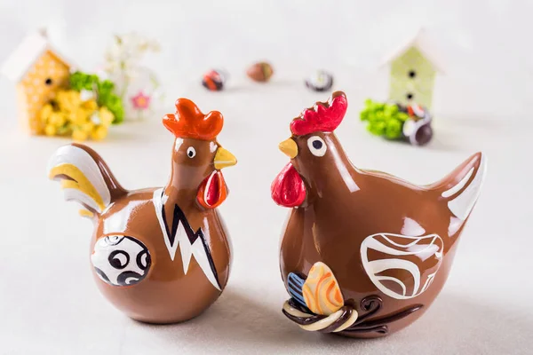 İki çikolatalı horoz, arka planda evleri var.