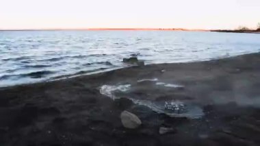 Laugarvatn, İzlanda 'daki jeotermal göl. Sert rüzgar eserken yerde sıcak su kabarcıkları oluşur. Siyah çakıl taşlı sahil boyunca sıcak buhar eser.