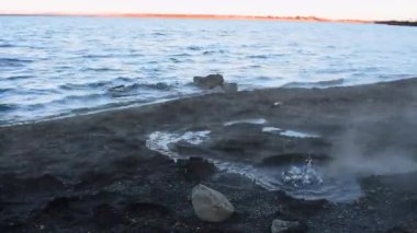 Laugarvatn, İzlanda 'daki jeotermal göl. Sert rüzgar eserken yerde sıcak su kabarcıkları oluşur. Siyah çakıl taşlı sahil boyunca sıcak buhar eser.