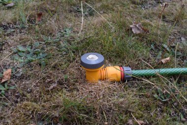 Bahçe hortumunun fıskiyesinin kapağı kuru ve sağlıksız çimenlerin üzerinde kullanılmadan duruyor. İngiltere kuraklığı, hortum yasağı.