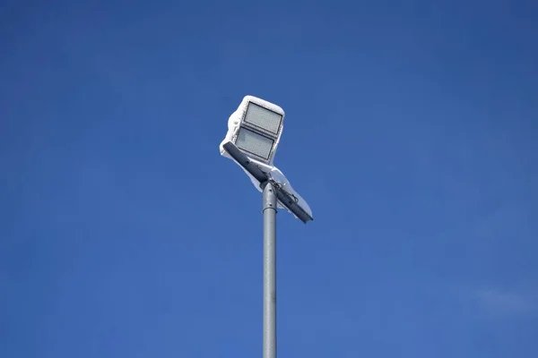 Snowy flood lights against a blue sky, used in skiing resort for flood lit skiing and snowboarding