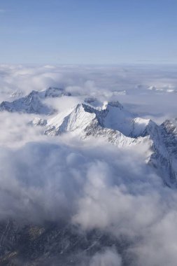 Ağır bulutların arasından yükselen dağlık dağ sırasının nefes kesen hava manzarası. Yukarıdan Otztal Alpleri 'nin dağ zirveleri. Etkileyici kış manzarası bir uçak penceresinden alınır..