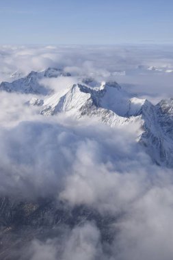 Ağır bulutların arasından yükselen dağlık dağ sırasının nefes kesen hava manzarası. Yukarıdan Otztal Alpleri 'nin dağ zirveleri. Etkileyici kış manzarası bir uçak penceresinden alınır..