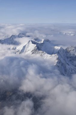 Breathtaking aerial view of alpine snowcapped mountain range peaking through heavy clouds. Mountain peaks of the Otztal Alps from above. The impressive winter view is taken from an airplane window. clipart