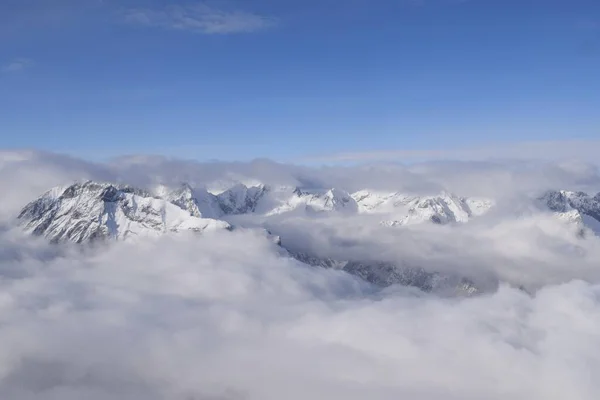 Ağır bulutların arasından yükselen dağlık dağ sırasının nefes kesen hava manzarası. Yukarıdan Otztal Alpleri 'nin dağ zirveleri. Etkileyici kış manzarası bir uçak penceresinden alınır..