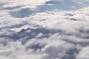 Ağır bulutların arasından yükselen dağ tepeli dağların rüya gibi hava manzarası. Yukarıdan Otztal Alpleri 'nin uzak dağ zirveleri. Etkileyici görüntü uçarken bir uçak penceresinden alınır..