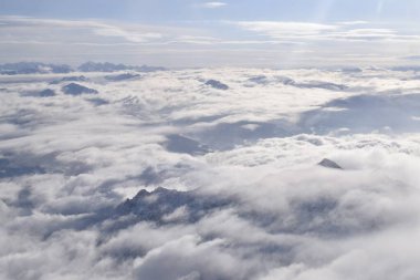 Ağır bulutların arasından yükselen dağ tepeli dağların rüya gibi hava manzarası. Yukarıdan Otztal Alpleri 'nin uzak dağ zirveleri. Etkileyici görüntü uçarken bir uçak penceresinden alınır..