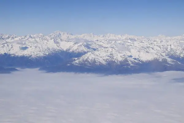 Karla kaplı dağ sırasının güzel hava manzarası ağır bulutların arasından yükseliyor. Yukarıdan, İtalyan Alpleri 'nin dağ zirveleri. Etkileyici kış manzarası bir uçak penceresinden alınır..