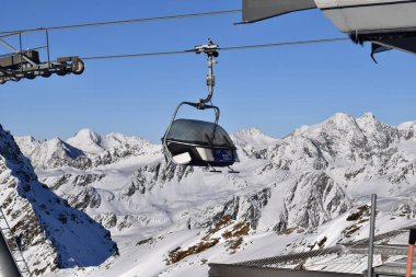 Avusturya, Tyrol 'daki Hochgurgl kayak merkezinin en üst istasyonunda boş sandalye asansörü. Güneşli bir kış gününde kayakçılar ve snowboardcular için Top Mountain Star 'a kaldırma. Karlı dağ zirvelerinin manzarası.