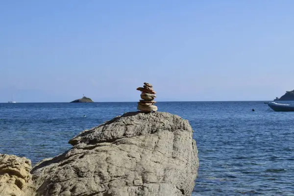 Balanced stack of rocks on a large, rough boulder on a beach on Skiathos island, Greece. Backdropped by the bright, calm aegean sea and a clear blue sky.