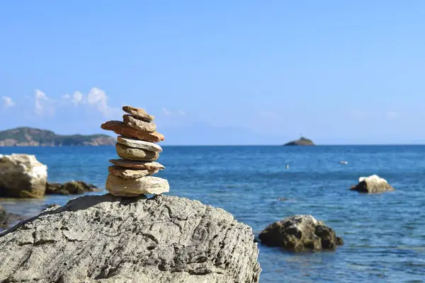 Balanced stack of rocks on a large, rough boulder on a beach on Skiathos island, Greece. Backdropped by the bright, calm aegean sea and a clear blue sky.
