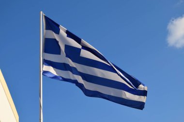 Mavi ve beyaz Yunan ulusal bayrağı açık mavi gökyüzüne doğru rüzgarda dalgalanıyor.