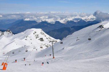 Kayakçılar ve snowboardcular Les Menuires kayak merkezindeki karlı pistlerde yokuş aşağı gidiyorlar. Üç vadideki karlı Fransız dağlarının zirvelerine bakan kış sporları aktiviteleri.