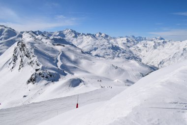 Kayakçılar ve snowboardcular Les Menuires kayak merkezindeki karlı pistlerde yokuş aşağı gidiyorlar. Üç vadideki karlı Fransız dağlarının zirvelerine bakan kış sporları aktiviteleri.